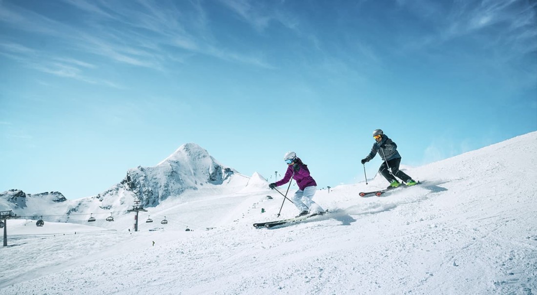 Zwei Skifahrer beim Gletscherskifahren fahren einen schneebedeckten Berg hinunter