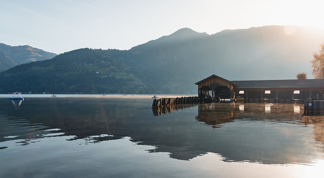 Zeller See mit einem Holzsteg und Bergen im Hintergrund bei Sonnenuntergang
