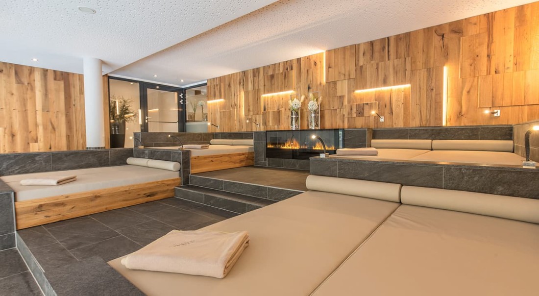 Gem&uuml;tlicher Wellnessbereich mit Liegen und Kamin vor h&ouml;lzerner Wand im Hotel Kaprunerhof