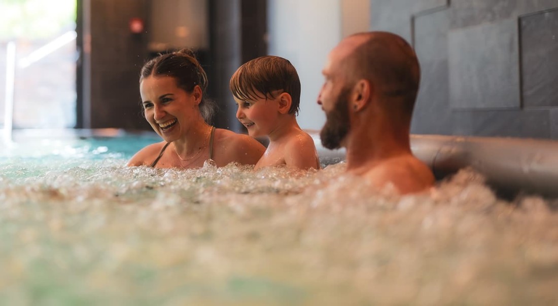 Eine Familie lacht gemeinsam auf den Sprudelliegen im Hallenbad im Hotel Kaprunerhof