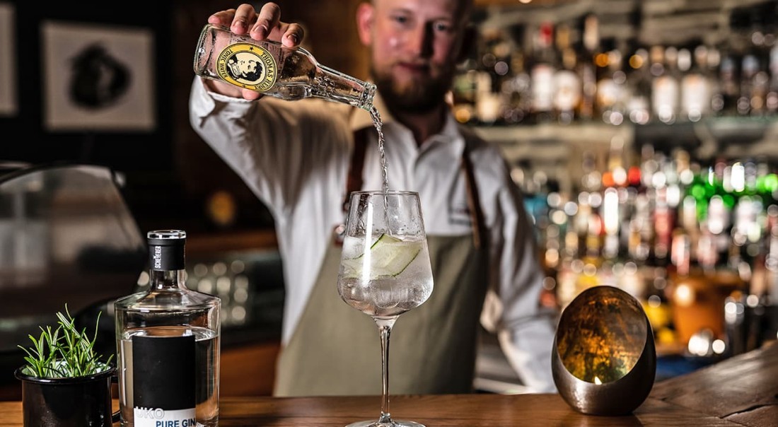Barkeeper gie&szlig;t Tonic ins Glas vor einer Regalwand voller Flaschen