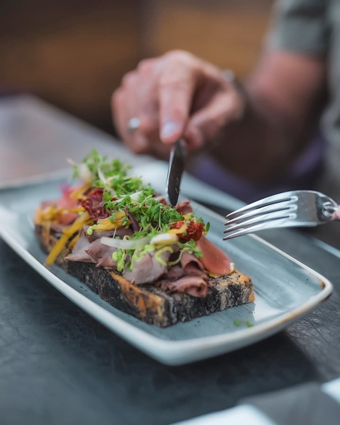 Ein belegtes Brot mit Schinken und Gem&uuml;se, das mit Besteck geschnitten wird