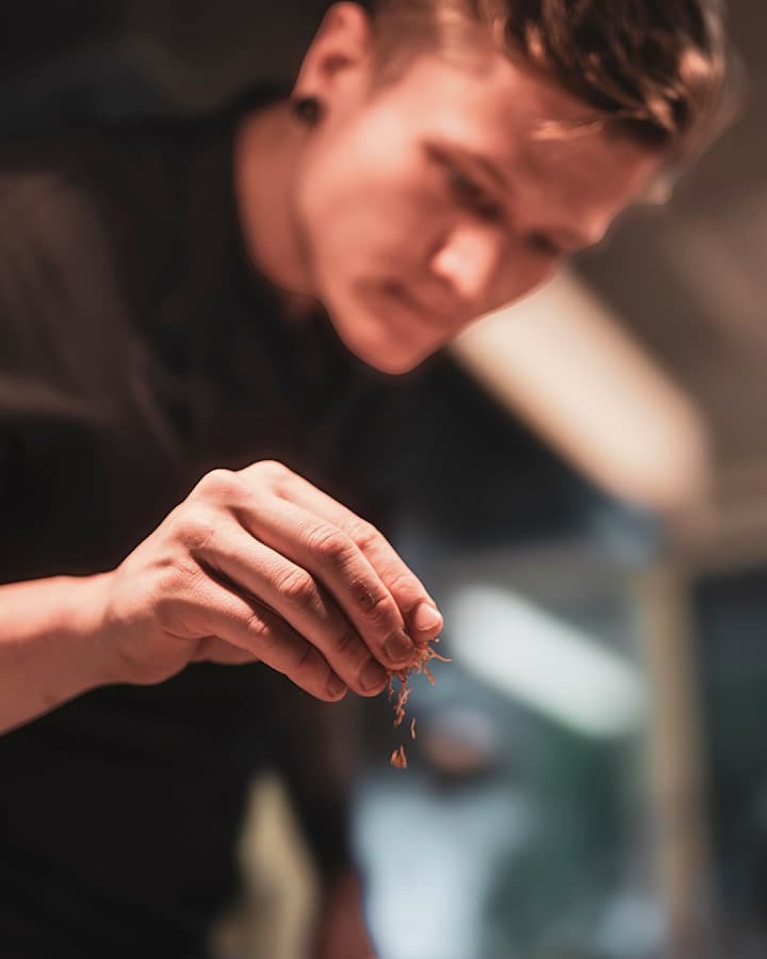 K&uuml;chenchef Stefan Unterkofler streut Gew&uuml;rze oder Kr&auml;uter aus der Hand in einem unscharfen Hintergrund