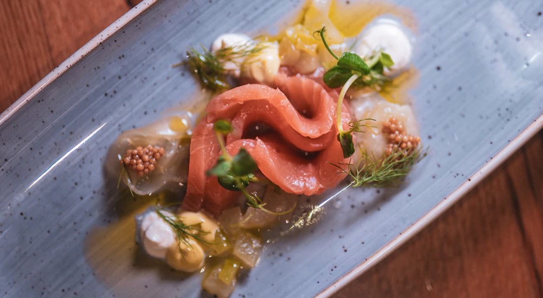 Gourmetgericht mit Lachs, Kr&auml;utern und So&szlig;en auf einem blauen, l&auml;nglichen Teller
