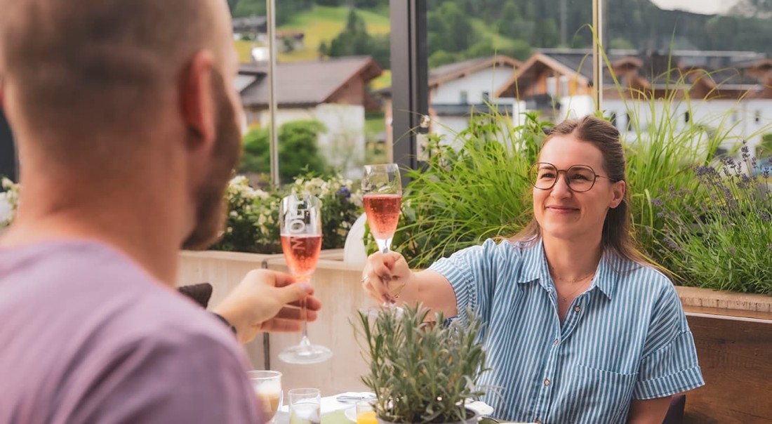 Zwei Personen sto&szlig;en an mit Sektgl&auml;sern auf der Sonnenterrasse beim Hotel Kaprunerhof