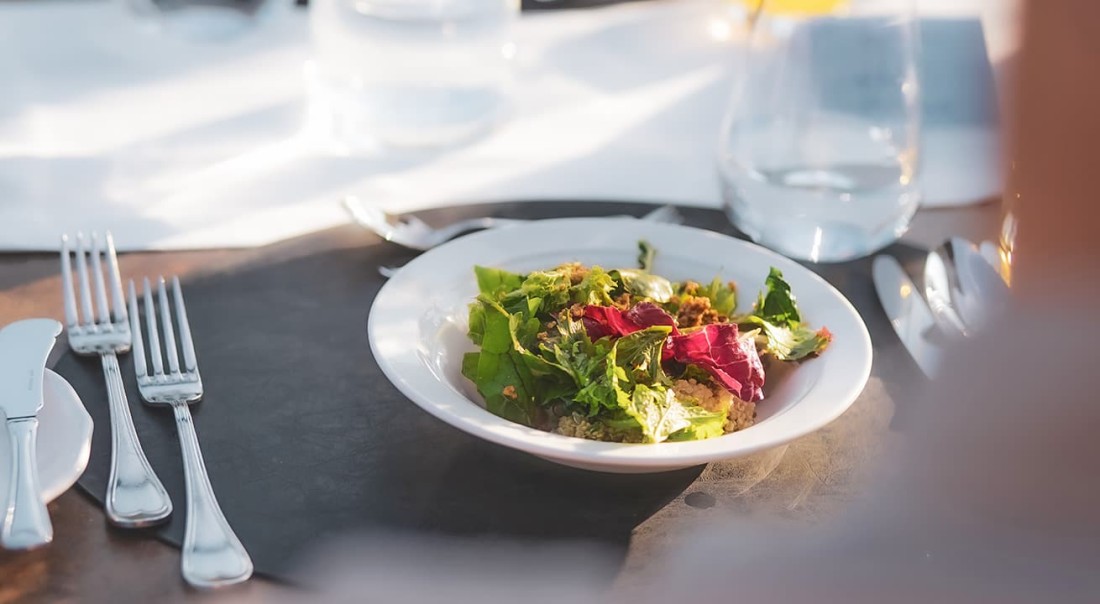 Ein Teller Salat steht auf einem gedeckten Tisch neben Besteck und einem Glas Wasser