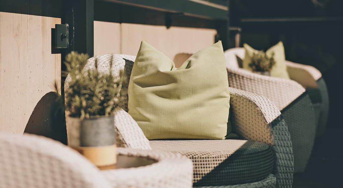 Wei&szlig;e Rattan-Sessel mit gr&uuml;nen Kissen und Pflanzen auf einer Terrasse