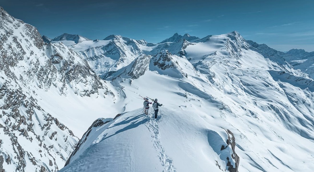 Zwei Personen stehen mit Skiern auf einem schneebedeckten Bergkamm am Kitzsteinhorn in den Alpen
