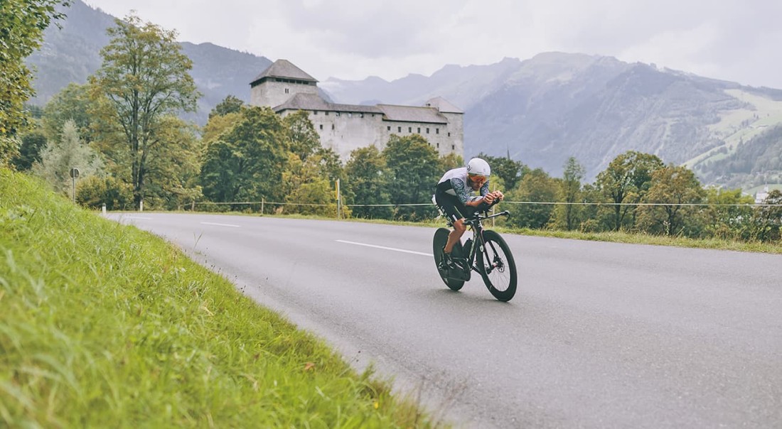 Radfahrer auf einsamer Stra&szlig;e vor einem Schloss und Bergen im Hintergrund