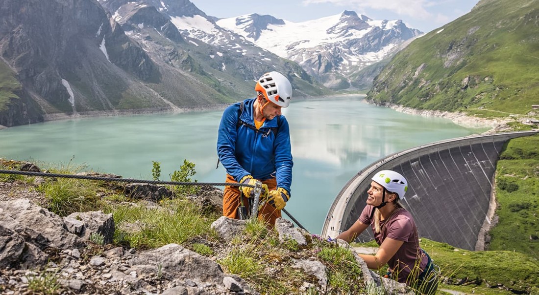 Zwei Personen klettern neben einem See und einer Staumauer Mooserboden in Kaprun in den Bergen