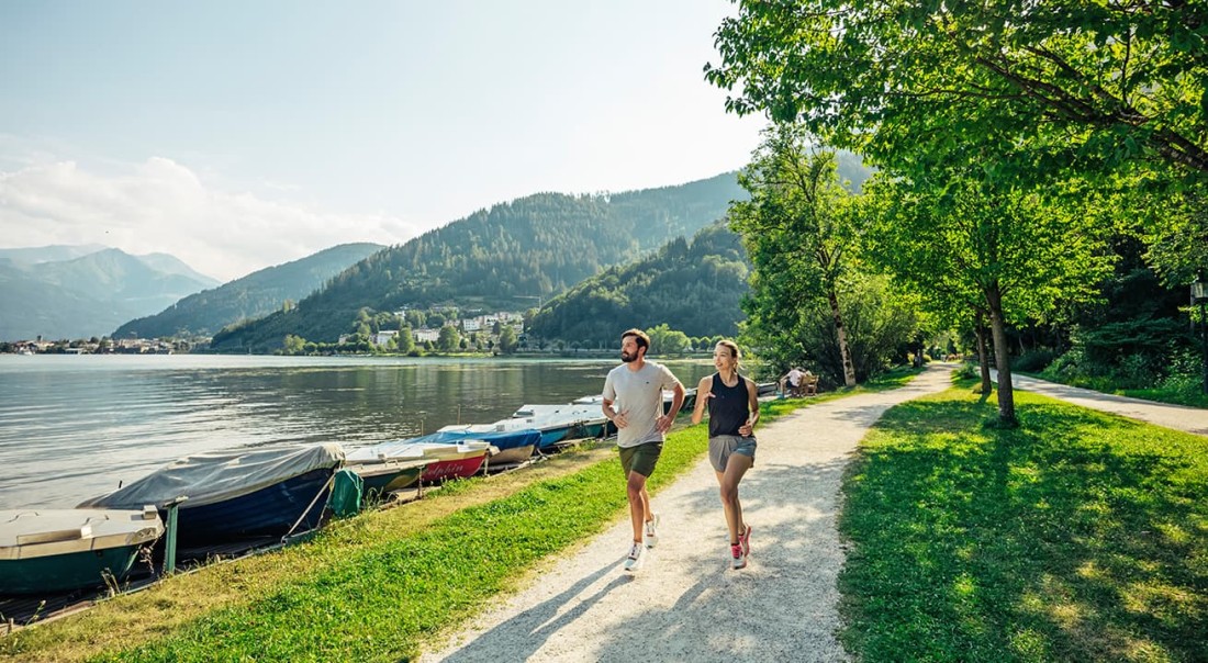 Zwei Personen joggen auf einem sonnigen Weg am Zeller See entlang