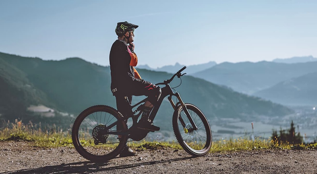 Ein Mountainbiker genie&szlig;t die Aussicht auf ein Tal vom Maiskogel und umgebende Berge