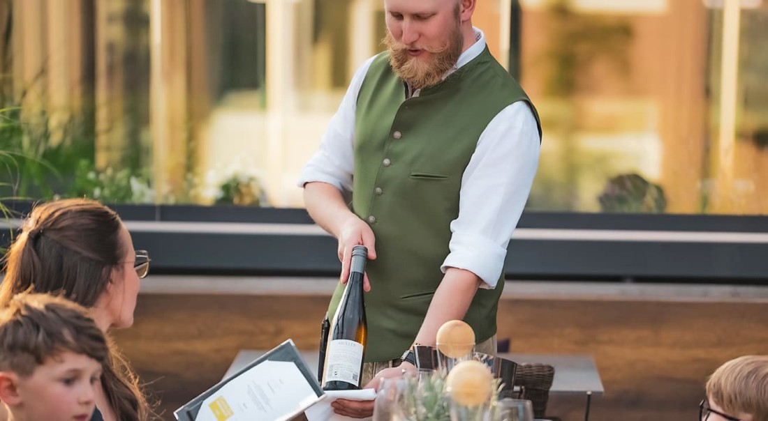 Ein Kellner vom Hotel Kaprunerhof pr&auml;sentiert G&auml;sten in einem Restaurant eine Flasche Wein