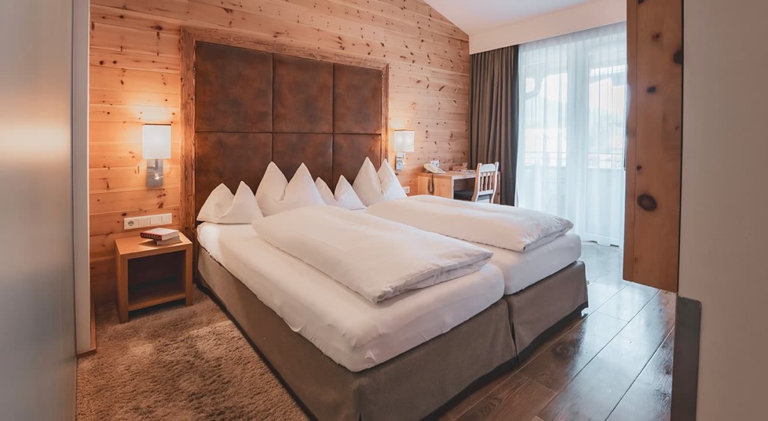 Helles Hotelzimmer mit Holzw&auml;nden, Doppelbett und Schreibtisch am Fenster