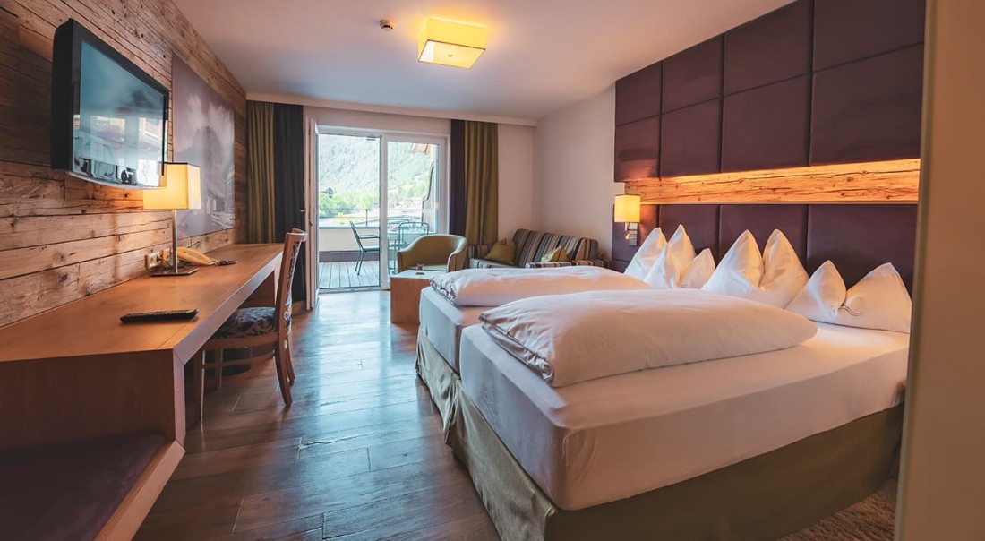 Hotelzimmer mit Doppelbett, Holzakzenten und Balkon mit Blick auf die Berge