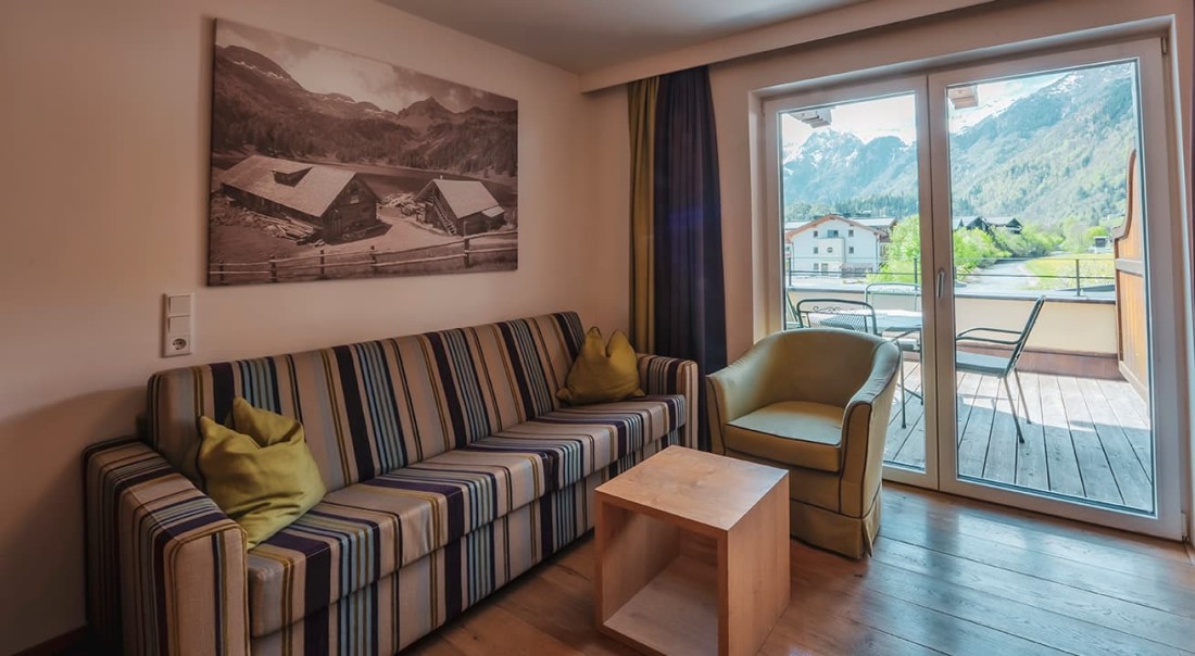 Sitzbereich mit gestreiftem Sofa, Sessel, kleinem Tisch und Blick auf Balkon und Berge