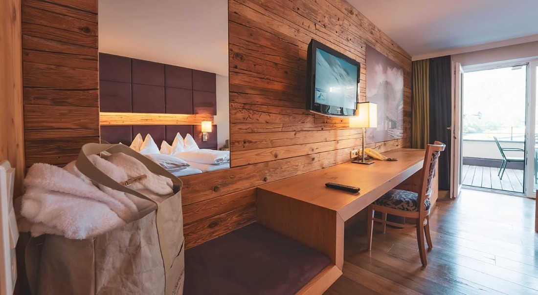 Gem&uuml;tliches Hotelzimmer mit Holzw&auml;nden, Schreibtisch, Fernseher und offenem Balkon