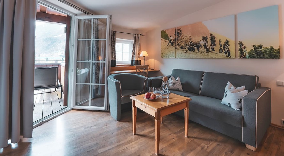 Gem&uuml;tliches Wohnzimmer mit grauem Sofa, Sesseln, Couchtisch und Zugang zum Balkon
