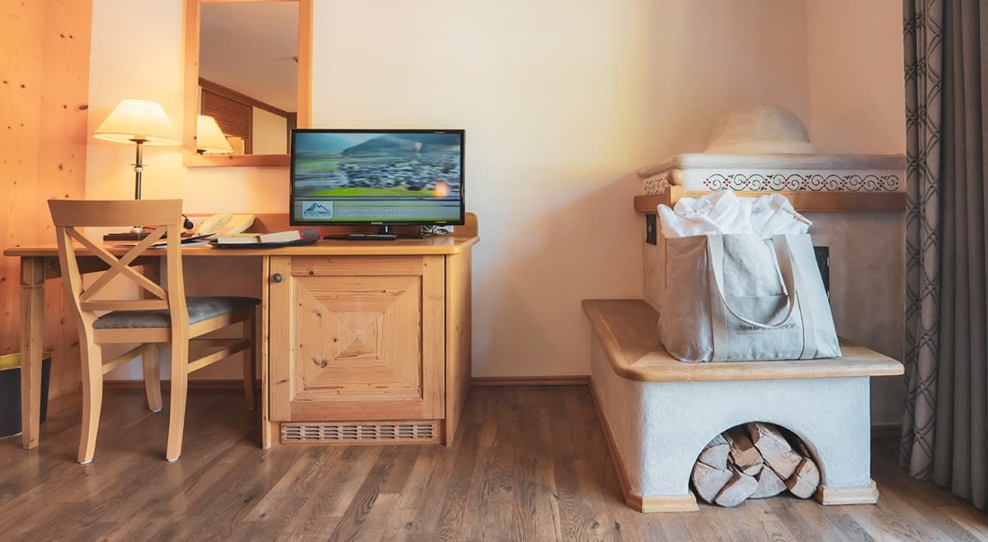 Ein gem&uuml;tlicher Raum mit Holzschreibtisch, Fernseher und traditionellem Kachelofen