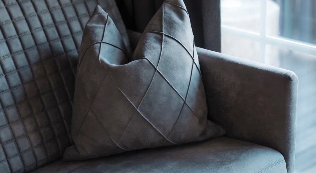 Graues Sofakissen mit Rautenmuster auf einem gepolsterten Sofa neben einem Fenster